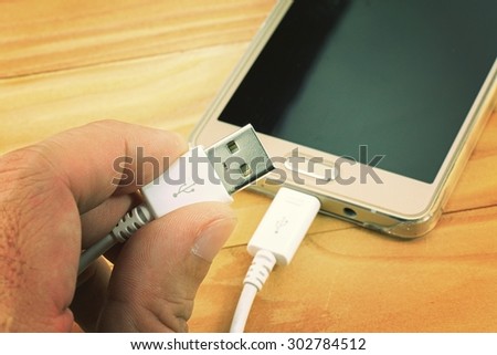 Hand holding USB connector, USB cable with smartphone on wood table.