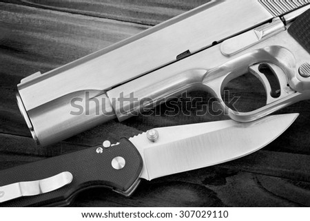 Semi-automatic handgun and tactical knife on wooden background, .45 pistol. (Black & White)