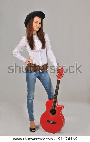A smiling girl in a black hat, white shirt, jeans and cowboy belt relies on red guitar