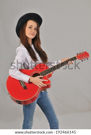 Girl in a black hat, white shirt, jeans and cowboy belt holding a red guitar in hand