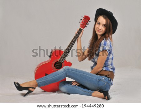 Young girl standing in a blouse with short sleeves, his right hand on the neck of the red guitar , and the left is based on a stretched forward with the right leg