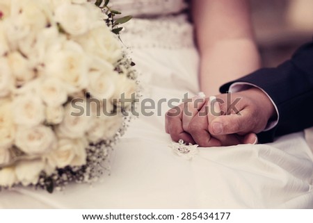 a close up of a bride and groom holding hands on their wedding day. Flowers in foreground and shallow depth of field. Vintage colour effect.
