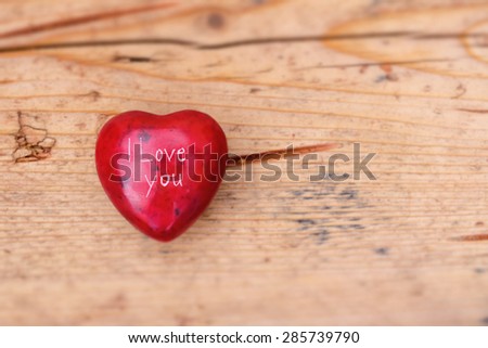 Red love heart with I LOVE YOU carved on the front resting on a light wooden aged backdrop. Shallow depth of field.