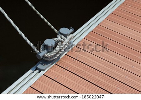 a mooring rope with a knotted end tightly tied around a cleat on a wooden pier/ Nautical mooring rope against dark blue sea water