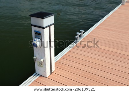 supply post for water, gas, electricity at the side of  footpath on a pier head with mooring cleats and berth of yacht marina on pontoons