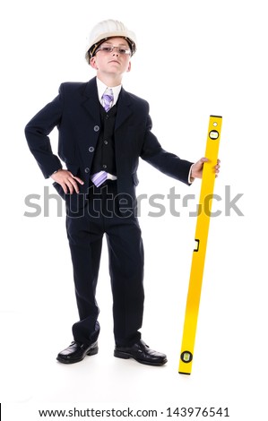Little boy in a dark suit wearing a white hard hat and wielding a yellow spirit level isolated against white background.
