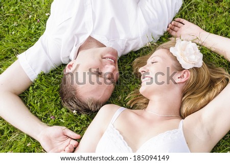 A young couple lying in grass on a summer meadow. You can see the heads in close-up from above perspective, the two look at love in the eyes.