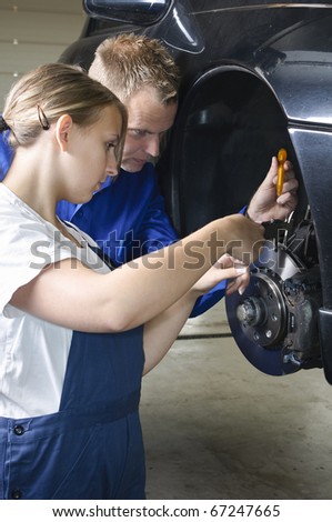 Auto mechanic shows the female trainee maintenance of the brakes in workshop in front of a car