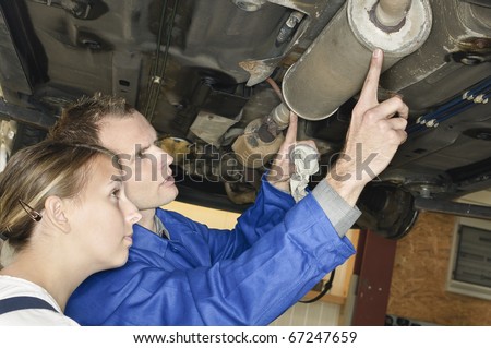 Auto mechanic shows the female trainee maintenance of the Car muffler under a car on a hoist