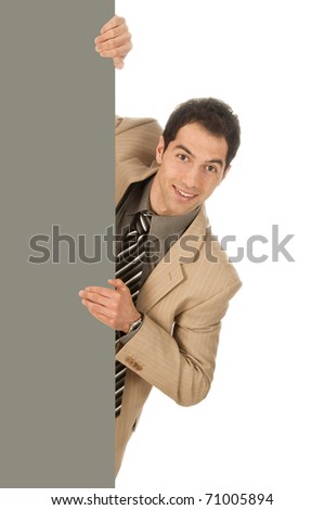 Young man in light suit looks smiling from behind a gray wall, isolated on a white background