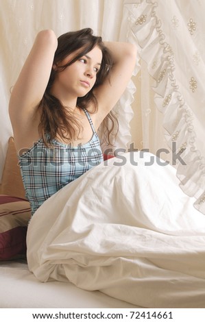 Young girl with long brunette hair rolls around in your pajamas on Sunday morning in the canopy bed.