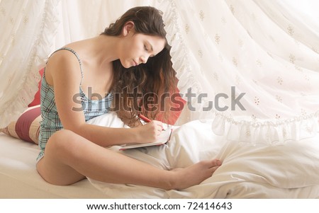 Young girl with long brunette hair rolls around in your pajamas on Sunday morning in the canopy bed, writing in her diary