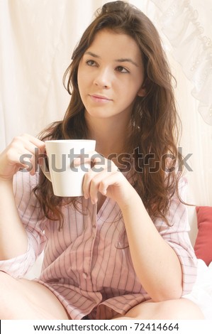 Young girl with long brunette hair rolls around in your pajamas on Sunday morning in the canopy bed, holding a large coffee cup in her hand