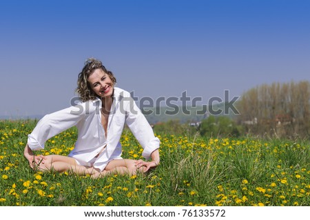 Atractive woman with blond hair and a white blouse to makes a rich flowering spring meadow yoga and relaxation exercises against a blue sky.
