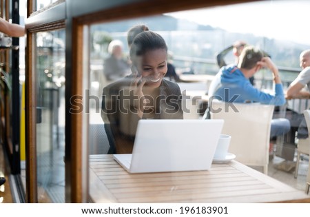 Young black businesswoman talking on the phone and using laptop in coffee shop