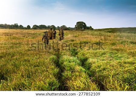 Group of people going into the distance on a green field with tall grass during sunrise