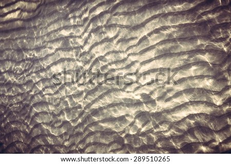 sandy bottom with reflecting sunlight from water ripples. Old fashioned style photography with darken edges