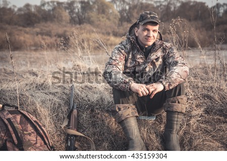 Hunter man in rural field with shotgun and backpack during hunting season