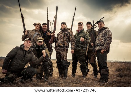Hunters standing together against sunrise sky in rural field during hunting season. Concept for teamwork.
