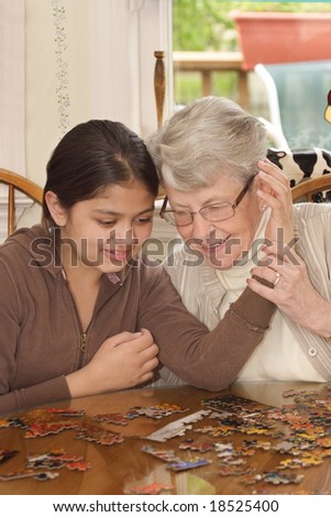 Grand daughter and grand mother with faces close together working on jigsaw puzzle on kitchen table