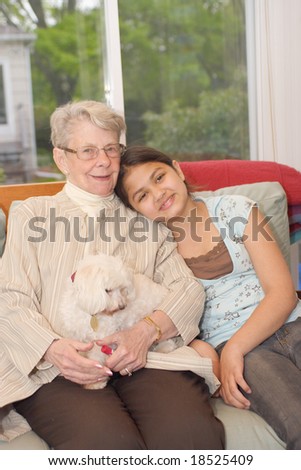 Grand daughter and grand mother with pet dog sitting on couch in sun room
