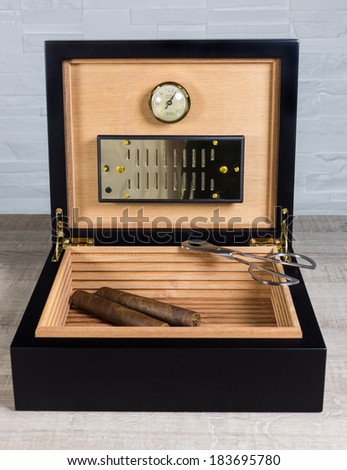Cigar humidor, vintage luxe cigar box and scissors on a wood table and white brick wall background