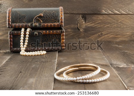 Pearl bracelet and vintage box with jewelry on color wooden background