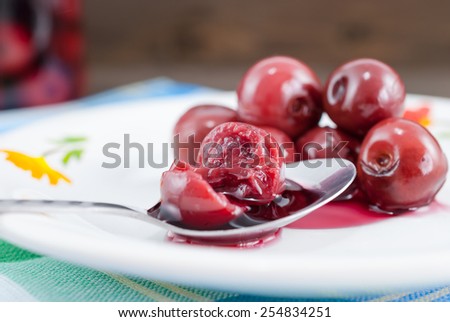 Close up of a sliced sour cherry on spoon along with other sour cherries taken out from a jar with compote