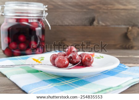 Sour cherries on spoon and in the background the jar with sour cherry compote