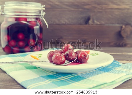 Vintage look of sour cherries on spoon and in the background the jar with sour cherry compote