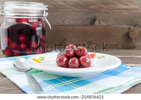 Sour cherries on white plate and in the background the jar with sour cherry compote