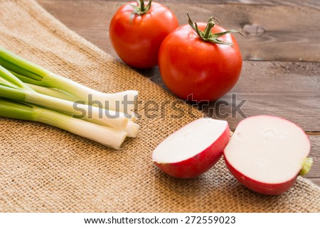 Green onion, tomatoes and sliced radish on burlap texture and wooden background. Concept for healthy eating