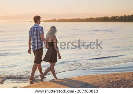 Young couple walk along the sea at sunset
