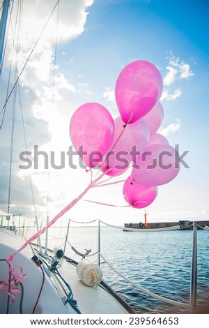 Pink balloons are waving in the wind on yacht in the sea at sunset