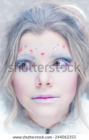 Beautiful young creative girl with white snowbound skin close up portrait in Snow Queen Character. Purple and Blue make up with pink rhinestones on forehead.
