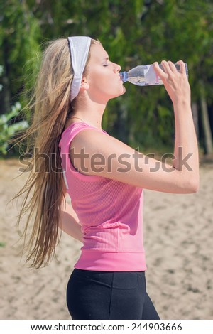 Young slim sporty girl drinks water after workout at sunny summer day