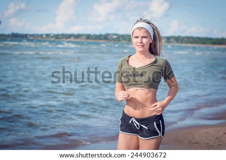 Young slim sporty girl runs along the sea shore at sunny summer day