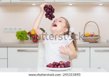 Sweet cute young girl with two ponytails smile and eat the fresh grapes.