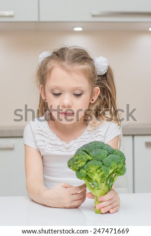 Little cute preschool girl don`t want to eat broccoli in the kitchen