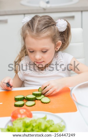 Little young cute sweet smiling girl make slices of cucumber