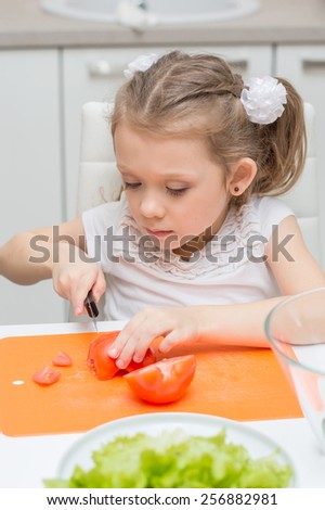 Little young cute sweet smiling girl make slices of tomatoes