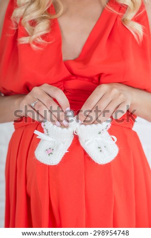 Pregnant woman  tummy with baby woolen knitted white socks in her hands