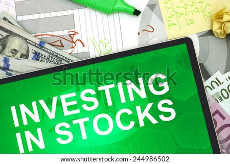 Tablet with words investing in stocks with dollars and euro. stocks concept