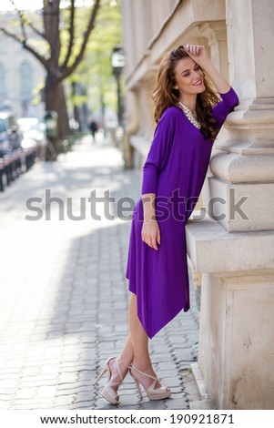 Beautiful young woman wearing a violet dress walking and posing