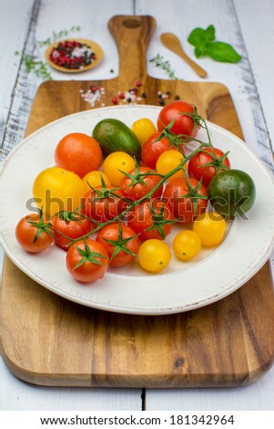 Freshly washed yellow, red, green and black tomatoes, herbs, salt and pepper on a vintage plate on a wooden cutting board