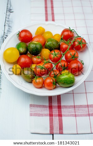 Freshly washed yellow, red, green and black tomatoes on a vintage plate on a painted white wooden surface covered with red-white kitchen towel