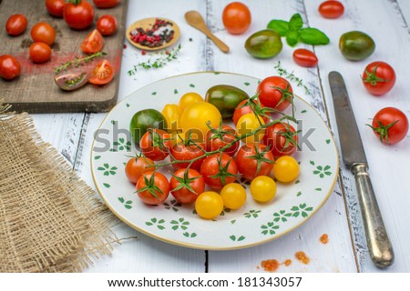 Freshly washed yellow, red, green and black tomatoes on a vintage plate, herbs, salt and pepper and a rusty knife on a shabby painted white wooden surface