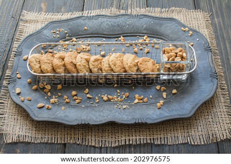 Peanut butter cookies and peanuts on large vintage plate on a surface of dark natural wood covered with canvas fabric