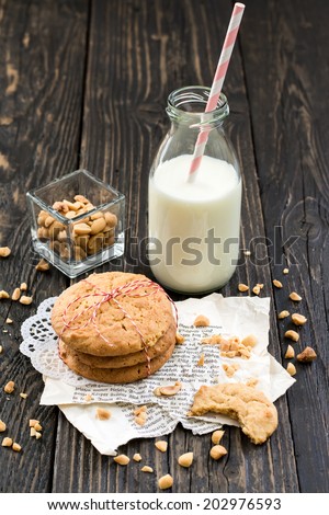 Peanut butter cookies, peanuts and a bottle of milk on a surface of dark natural wood