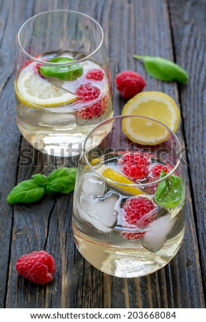 Raspberry basil cocktail with sparkling white wine, elderberry syrup, a slice of lemon and ice cubes on a natural wood surface
